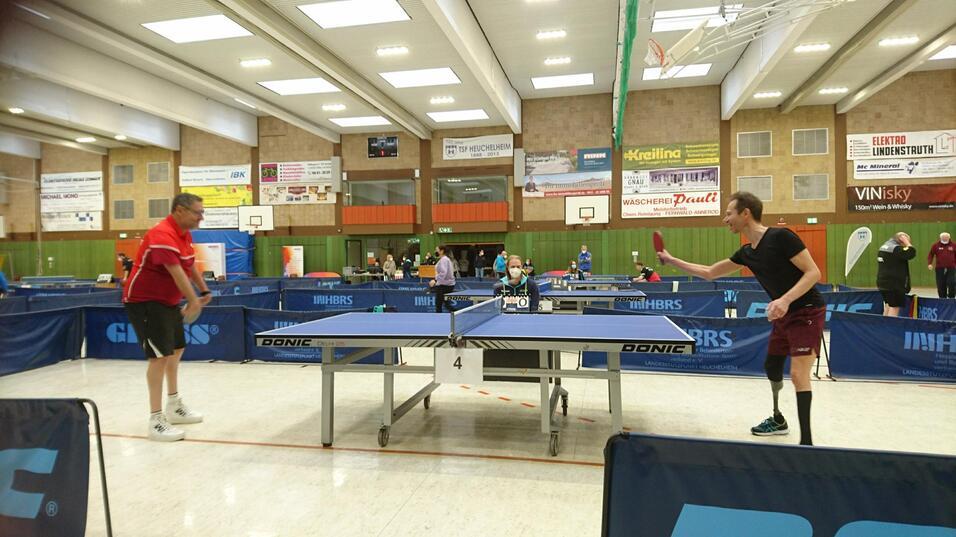 Zwei Tischtennisspieler in einem Sportzentrum stehen sich an einem Tisch gegen&uuml;ber, bereit f&uuml;r den Aufschlag.