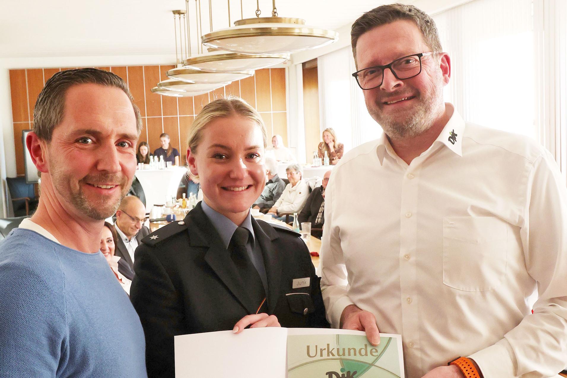 Drei Personen in einem Raum halten gemeinsam eine Urkunde mit der Aufschrift &bdquo;Urkunde DIK&ldquo;.