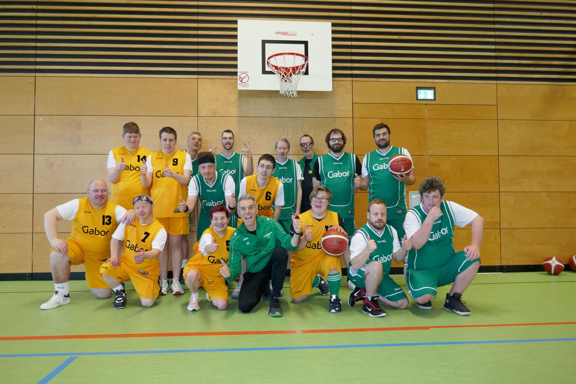 Gruppe von Basketballspielern in gelben und gr&uuml;nen Trikots posiert gemeinsam auf einem Basketballfeld.