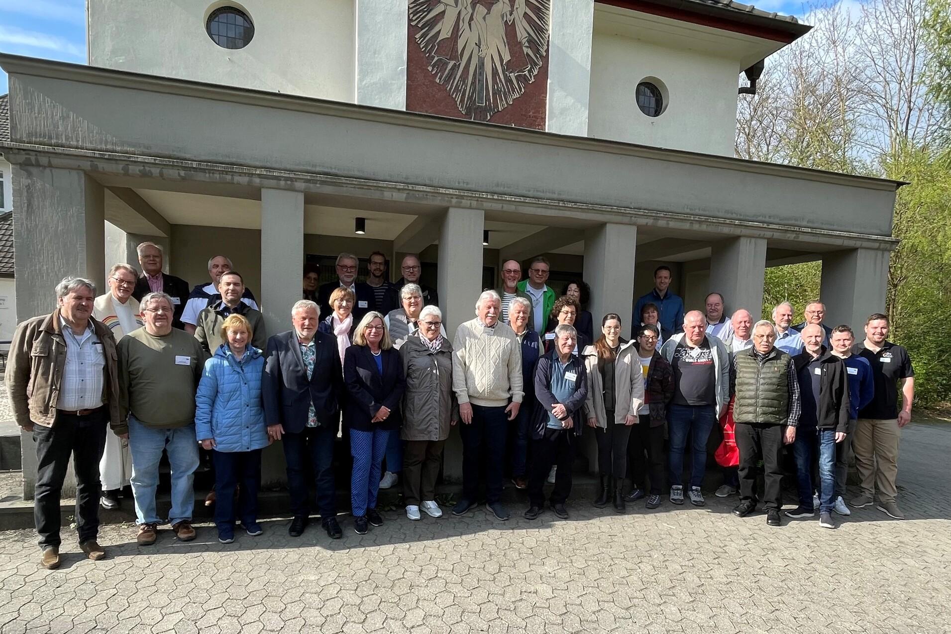 Gruppenfoto von ca. 40 Personen vor einem Geb&auml;ude mit einem Wappen im Hintergrund an einem sonnigen Tag.