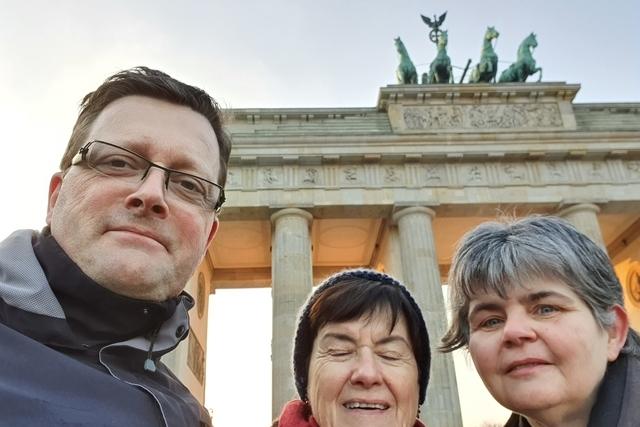 Drei Personen posieren vor dem Brandenburger Tor im Hintergrund, bei Sonnenaufgang in Berlin.