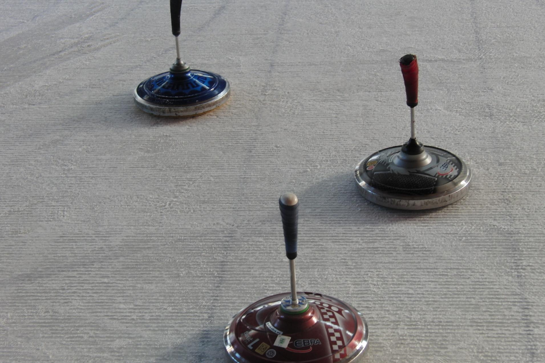 Drei bunte Kreisel stehen auf einem glatten, hellen Untergrund.