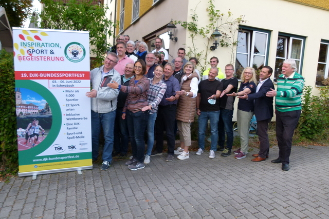 Gruppe von Menschen posiert fr&ouml;hlich vor einem Plakat zum DJK-Bundessportfest in Schwabach.