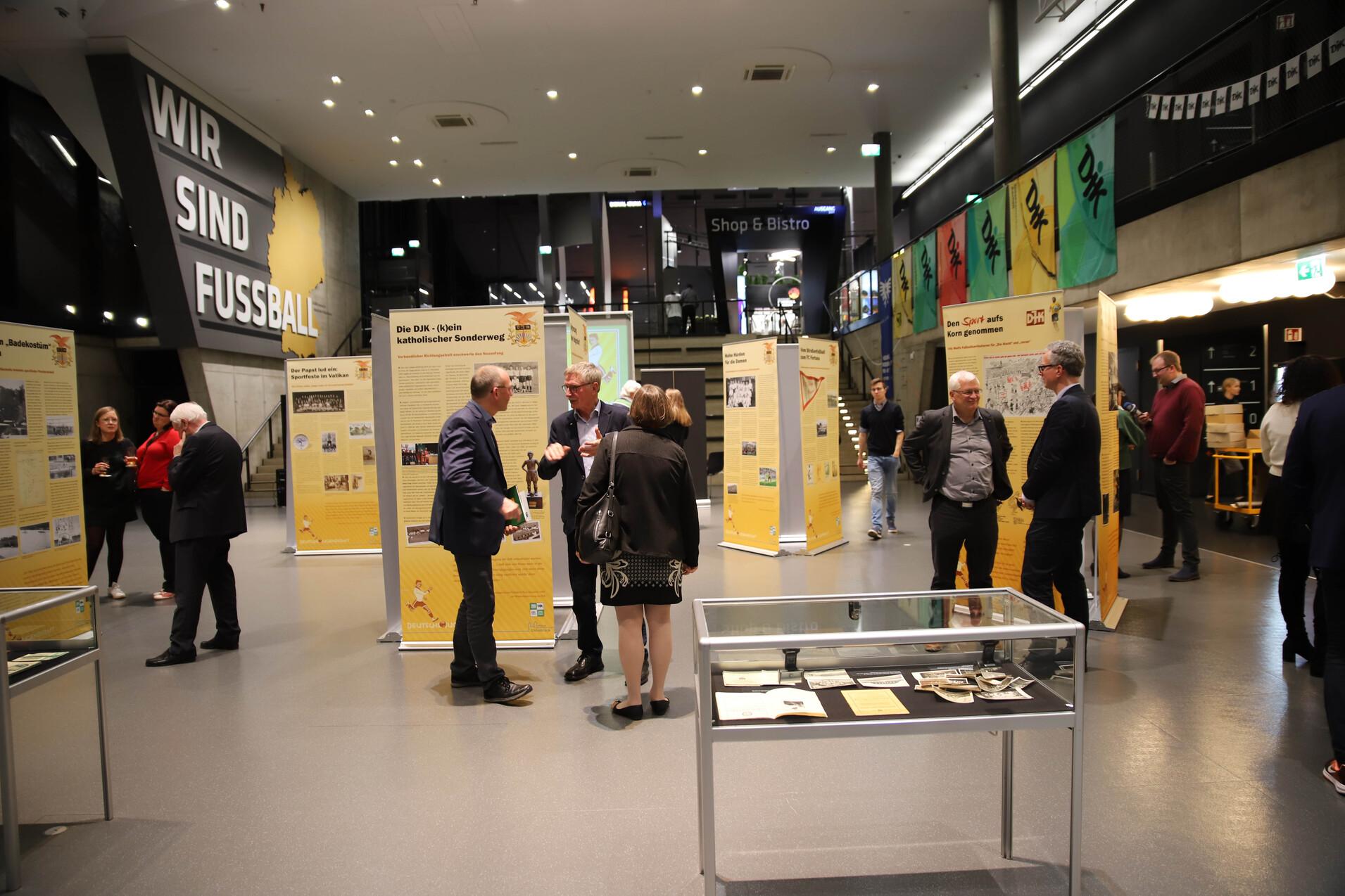 Ausstellung im Fu&szlig;ballmuseum mit Besuchern, Informationsst&auml;nden und einem Glasvitrinen in der Mitte des Raumes.