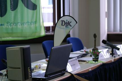 Tisch mit Laptop, Mikrofon und Dekorationsblumen, im Hintergrund ein Banner des Sportverbands.