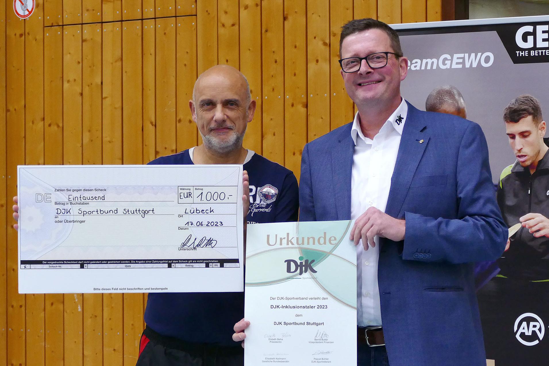 Zwei M&auml;nner stehen nebeneinander und halten einen gro&szlig;en Scheck sowie eine Urkunde des DJK Sportbund Stuttgart.