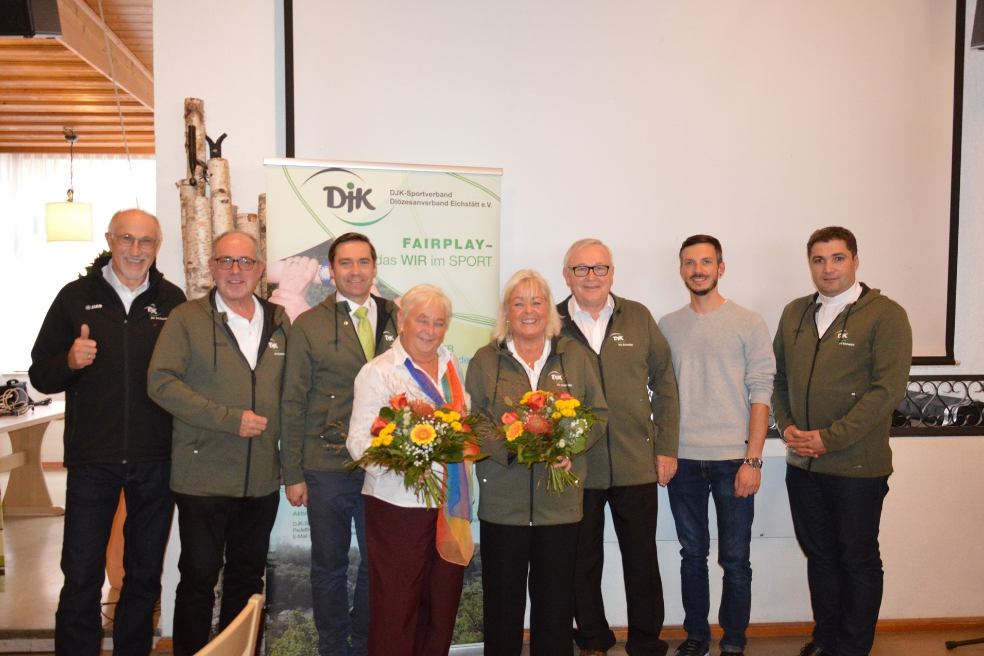 Gruppe von sieben Personen in sportlicher Kleidung stehen vor einem Banner mit der Aufschrift "Fairplay &ndash; das wir im Sport".
