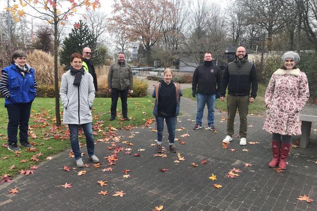 Gruppe von acht Personen steht in einem herbstlichen Park, umgeben von bunten Laubbl&auml;ttern.