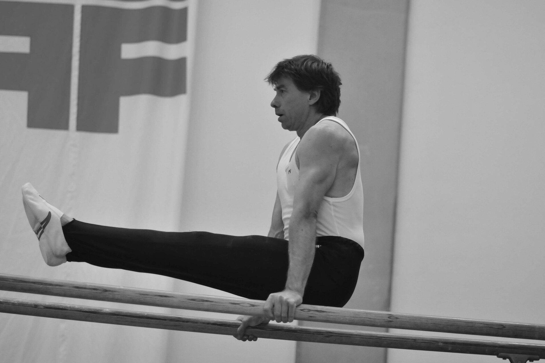 Mann in sportlichem Oberteil f&uuml;hrt einen St&uuml;tz an einem Barren in einem Sportstudio aus.