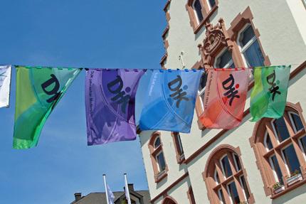 Bunte Fahnen mit chinesischen Schriftzeichen h&auml;ngen vor einem historischen Geb&auml;ude unter blauem Himmel.