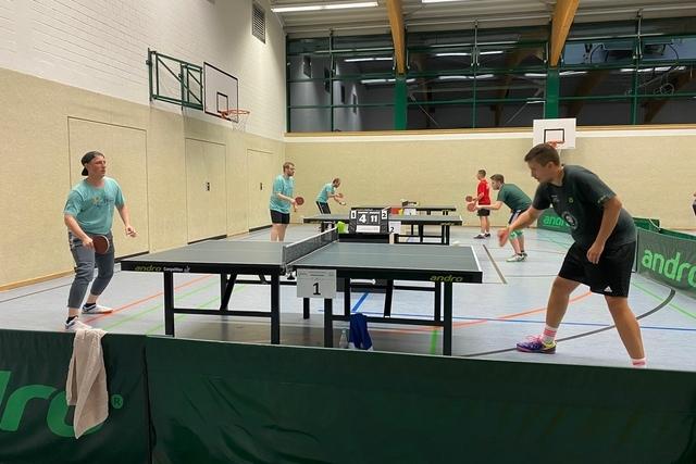 Gruppentraining im Tischtennis mit Spielern an mehreren Tischen in einer Sporthalle.