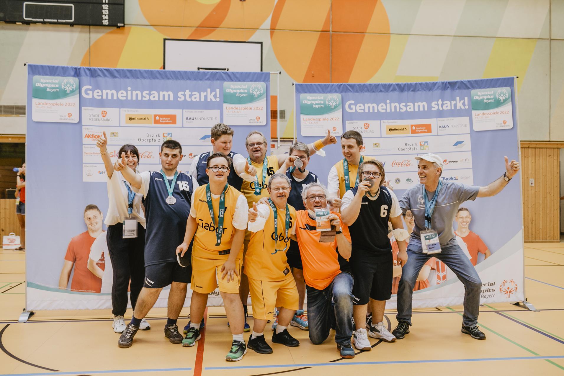 Gruppe von sportlichen Teilnehmern mit Medaillen und Pokal, posierend vor Bannern mit dem Schriftzug &bdquo;Gemeinsam stark!&ldquo;