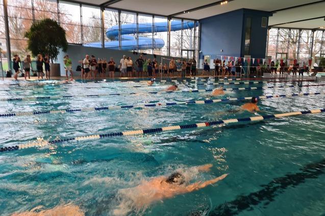 Wettkampf im Schwimmbecken mit mehreren Schwimmern und Zuschauern, im Hintergrund eine Wasserrutsche.