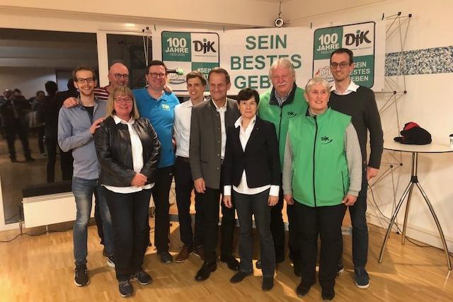 Gruppenfoto von zehn Personen in einem Raum, mit Plakat im Hintergrund, das f&uuml;r ein Jubil&auml;um wirbt.