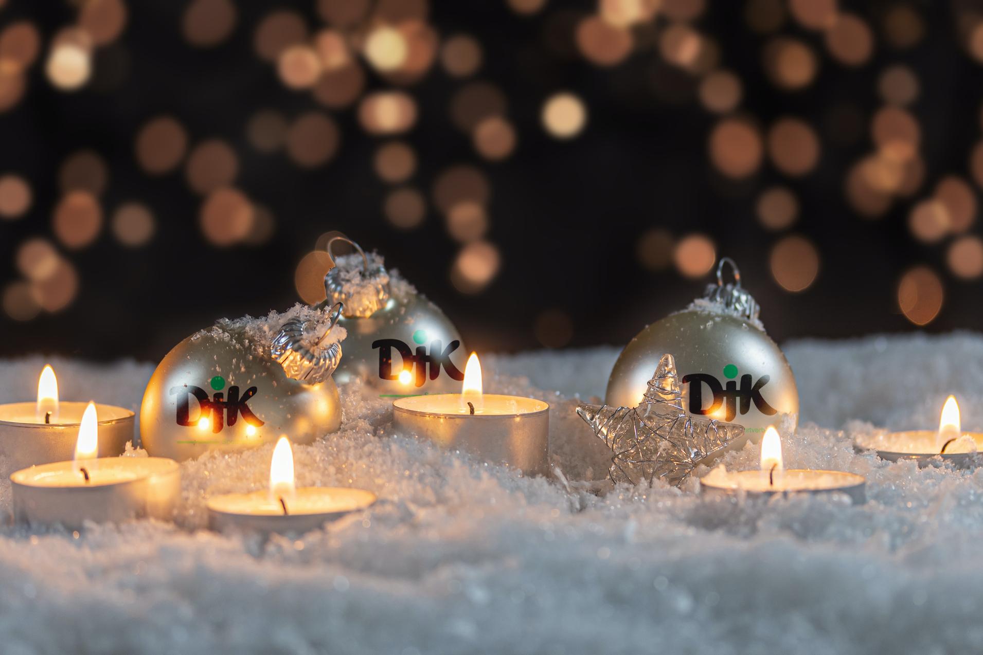 Drei silberne Weihnachtskugeln und Teelichter stehen auf glitzerndem Schnee vor einem verschwommenen Lichthintergrund.