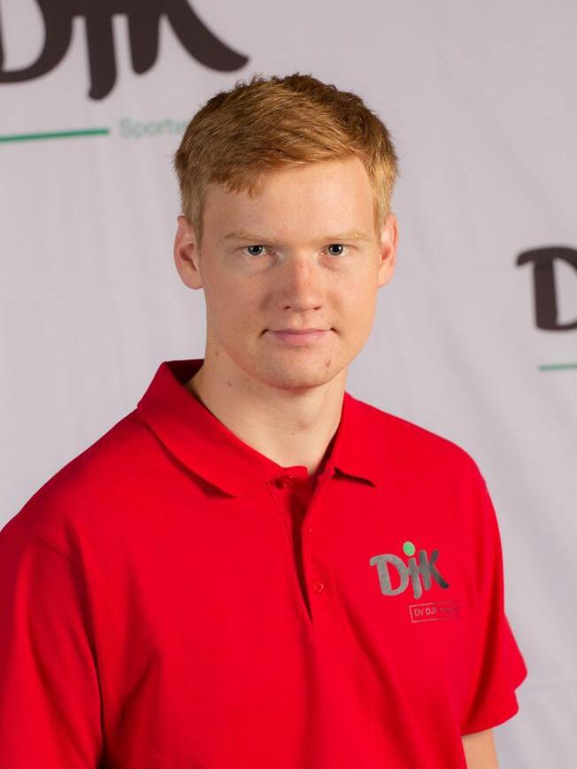 Portr&auml;t eines jungen Mannes in einem roten Poloshirt mit dem Logo &bdquo;DJK&ldquo; vor einem neutralen Hintergrund.