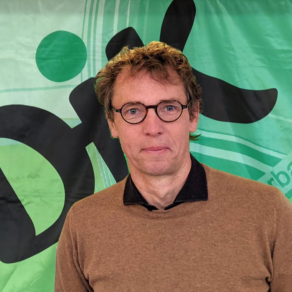 Mann mit Brille steht vor einem gr&uuml;nen Hintergrund mit dem Wort "Dix" in schwarzer Schrift.