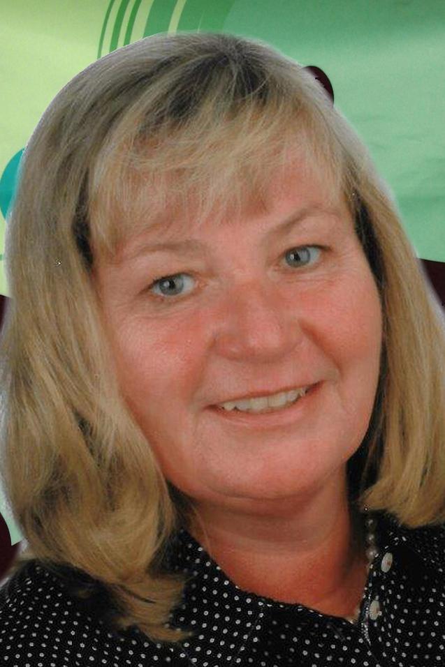 Portr&auml;t einer l&auml;chelnden Frau mit blonden, glatten Haaren und blauer Bluse vor einem bunten, gr&uuml;nen Hintergrund.