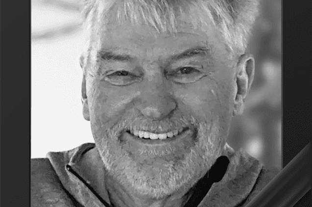 Portr&auml;t eines l&auml;chelnden Mannes mit grauen Haaren in einem grauen Sweatshirt, eingerahmt mit einer schwarzen Trauerschleife.