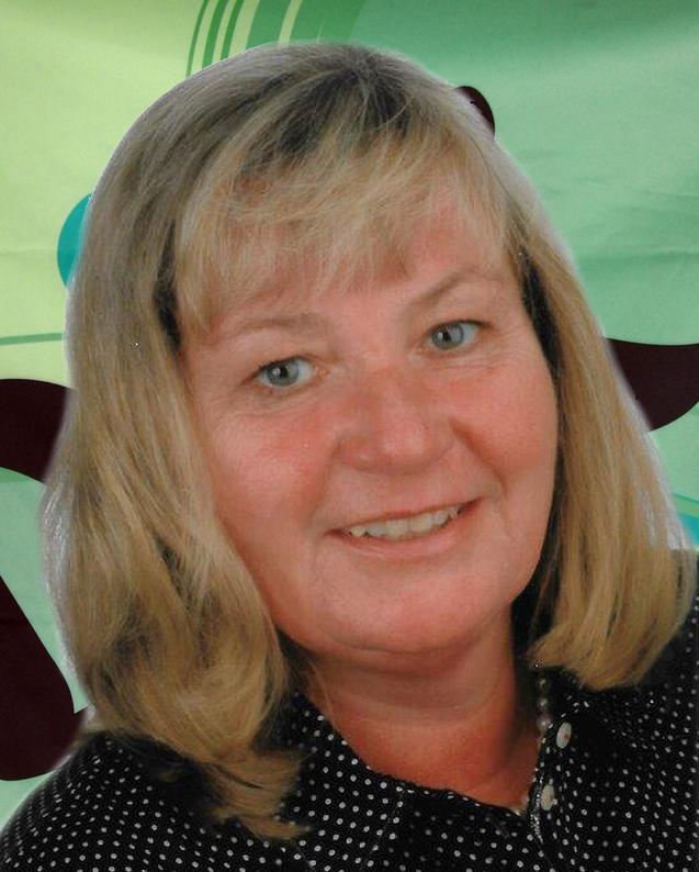 Portr&auml;t einer l&auml;chelnden Frau mit blonden, glatten Haaren und blauer Bluse vor einem bunten, gr&uuml;nen Hintergrund.