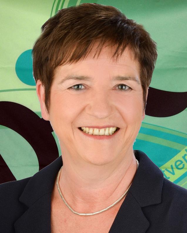 Portr&auml;t einer l&auml;chelnden Frau mit kurzem, braunem Haar, in einem dunkelblauen Blazer vor einem bunten Hintergrund.