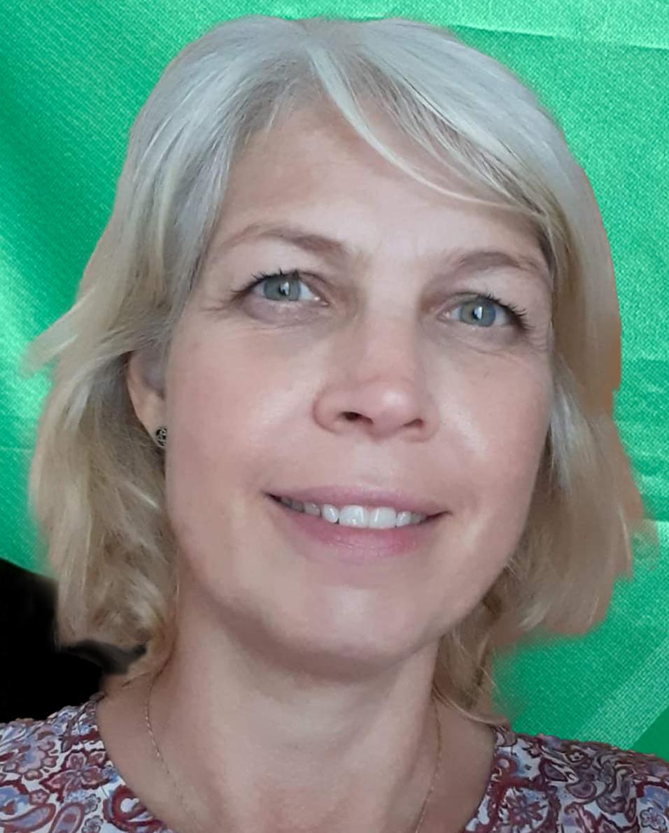 Portr&auml;t einer l&auml;chelnden Frau mit blonden Haaren vor einem gr&uuml;nen Hintergrund. Sie tr&auml;gt ein gemustertes Oberteil.