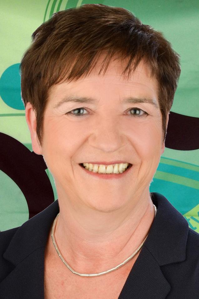 Portr&auml;t einer l&auml;chelnden Frau mit kurzem, braunem Haar, in einem dunkelblauen Blazer vor einem bunten Hintergrund.