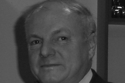 Portr&auml;t eines Mannes mit blonden Haaren, in einem Anzug, vor unscharfem Hintergrund.