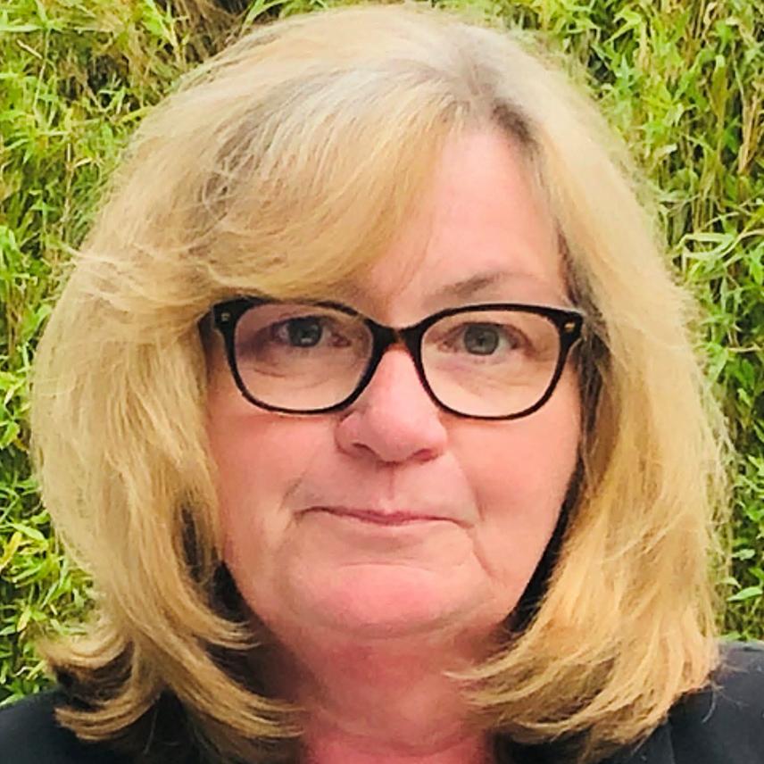 Frau mit blonden, schulterlangen Haaren und Brille, vor gr&uuml;nem Hintergrund.