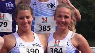 Zwei Athletinnen in wei&szlig;en Trikots stehen l&auml;chelnd nebeneinander, mit Startnummern auf der Brust.