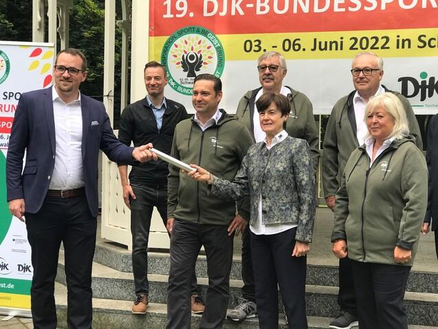 Gruppenfoto von mehreren Personen, die eine Feierlichkeit zum 19. DJK-Bundessporttag mit einer &Uuml;bergabe im Freien zeigen.