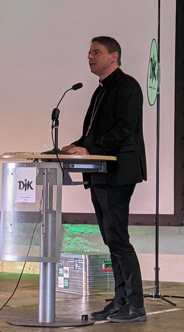 Mann in schwarzer Kleidung steht an einem Rednerpult mit Mikrofon auf einer B&uuml;hne w&auml;hrend einer Veranstaltung.