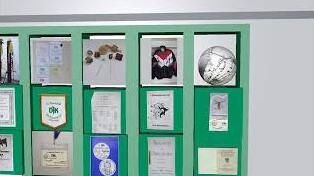 Sammlung von Urkunden, Medaillen und einem Trikot in einem gr&uuml;nen Vitrinenschrank.