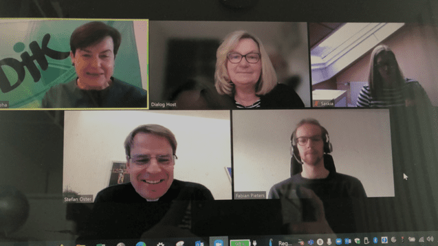 Videokonferenz mit f&uuml;nf Personen, darunter eine Frau mit gr&uuml;nem Oberteil und vier weitere Teilnehmer in unterschiedlichen Outfits.