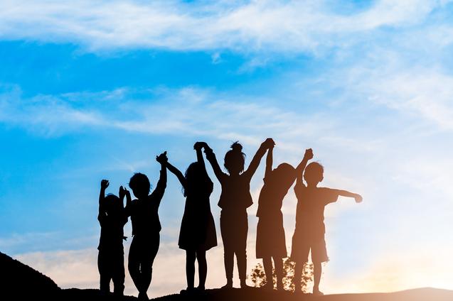 Silhouette von sechs Kindern, die bei Sonnenuntergang jubelnd die Arme heben, vor einem blauen Himmel.