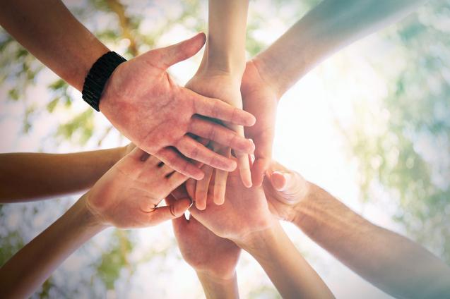 Eine Gruppe von H&auml;nden verschiedener Menschen legt sich &uuml;bereinander, eingefangen aus einer erh&ouml;hten Perspektive.