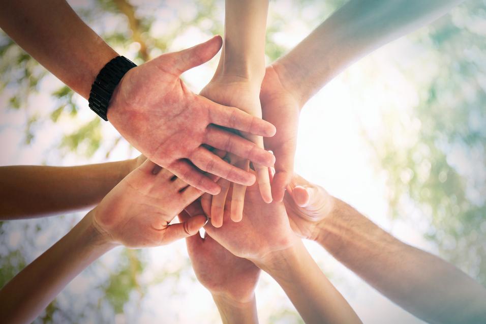 Eine Gruppe von H&auml;nden verschiedener Menschen legt sich &uuml;bereinander, eingefangen aus einer erh&ouml;hten Perspektive.