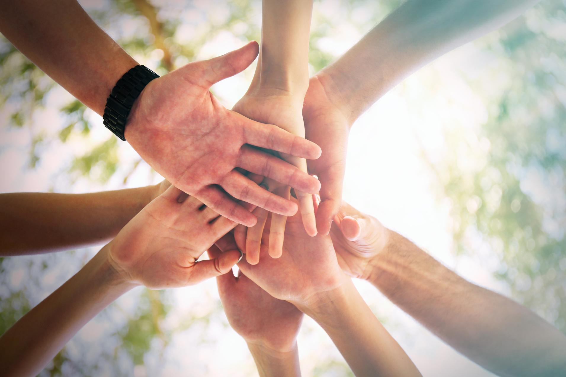 Eine Gruppe von H&auml;nden verschiedener Menschen legt sich &uuml;bereinander, eingefangen aus einer erh&ouml;hten Perspektive.