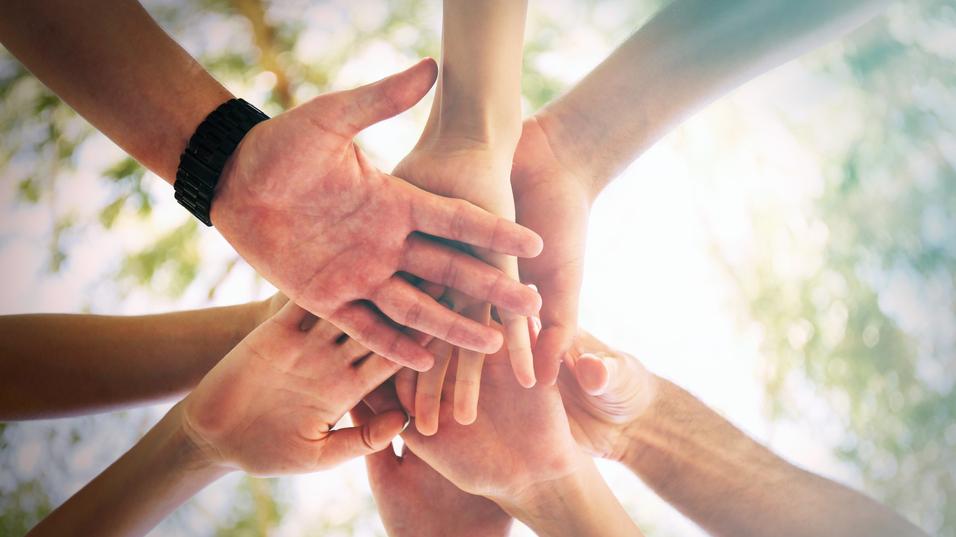 Eine Gruppe von H&auml;nden verschiedener Menschen legt sich &uuml;bereinander, eingefangen aus einer erh&ouml;hten Perspektive.