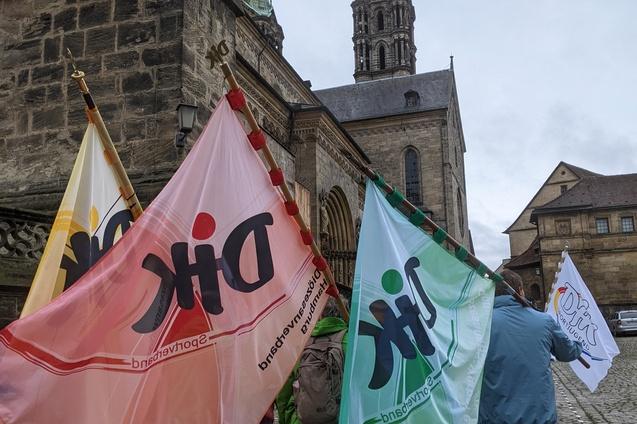 Menschen mit Fahnen in rot, gr&uuml;n und wei&szlig; gehen an einer historischen Kirche vorbei.