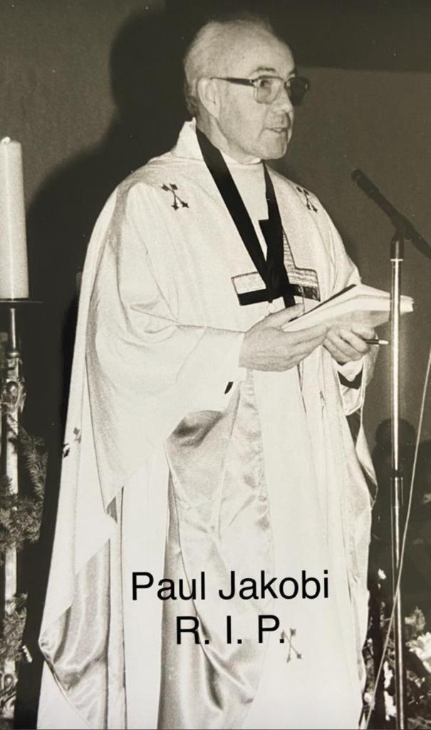 Ein Priester in liturgischer Kleidung steht mit einem Buch in der Hand, w&auml;hrend er eine Ansprache h&auml;lt.