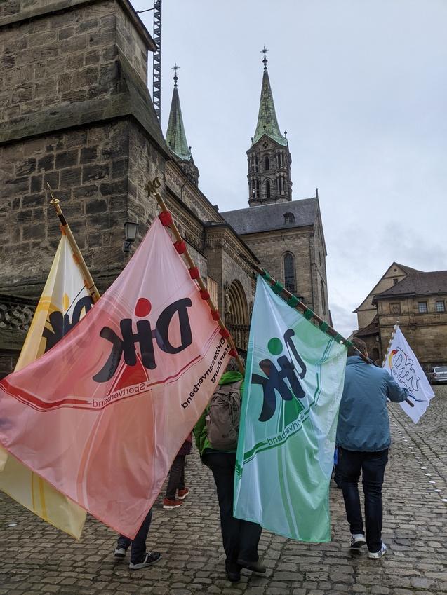 Menschen mit Fahnen in rot, gr&uuml;n und wei&szlig; gehen an einer historischen Kirche vorbei.