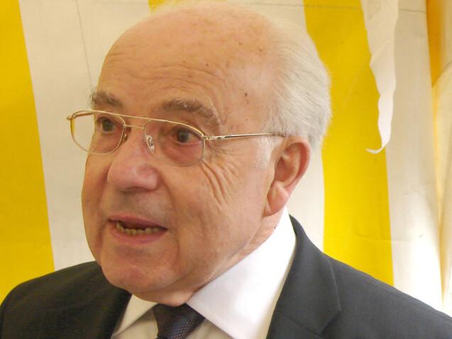 &Auml;lterer Mann mit Brille spricht leidenschaftlich vor gelb-wei&szlig; gestreiften Hintergrund.