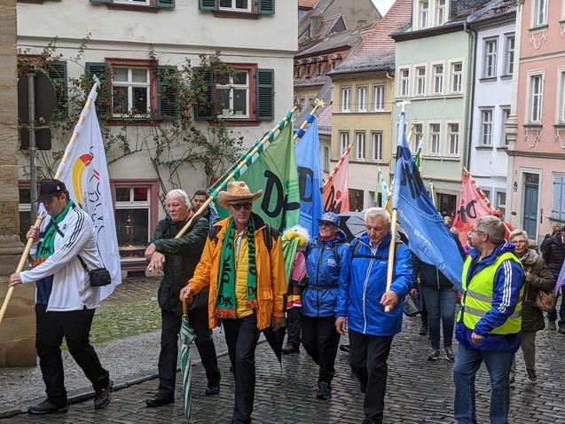 Gruppierung von Menschen mit Fahnen marschiert durch eine enge Stra&szlig;enansicht mit historischen Geb&auml;uden.
