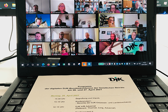 Screenshot einer Videokonferenz mit mehreren Teilnehmern auf einem Laptop, darunter das Programmheft der Veranstaltung.