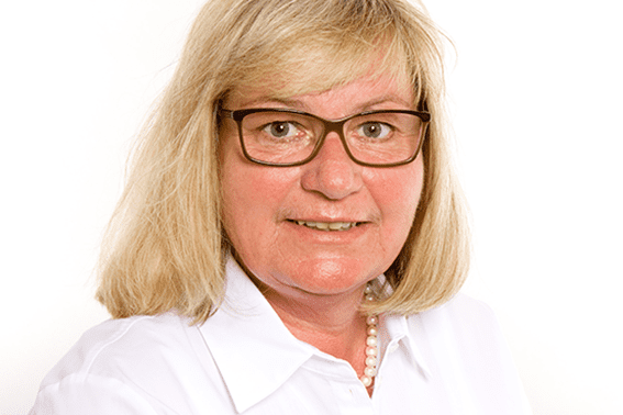 Portr&auml;t einer l&auml;chelnden Frau mit blonden Haaren und Brille, die ein wei&szlig;es Hemd tr&auml;gt, vor einem wei&szlig;en Hintergrund.