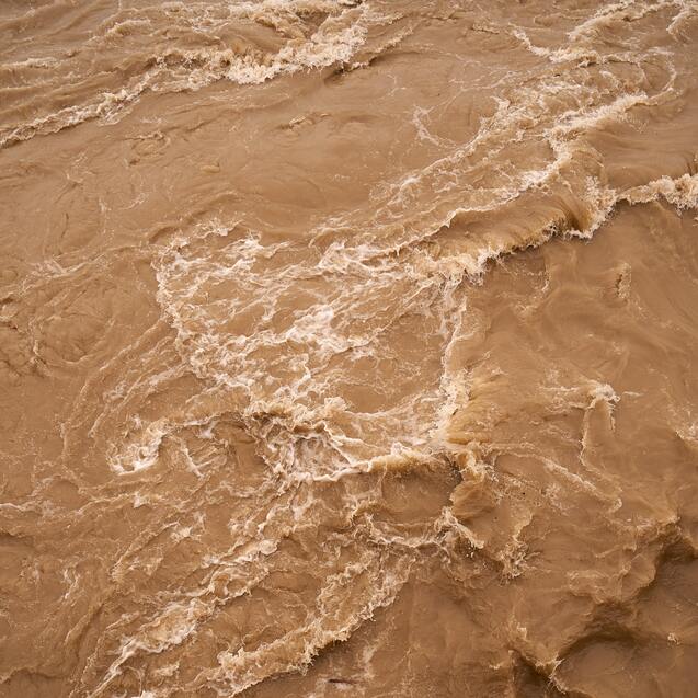 Braun gef&auml;rbtes Wasser mit sch&auml;umenden Wellen flie&szlig;t turbulent &uuml;ber eine Fl&auml;che.