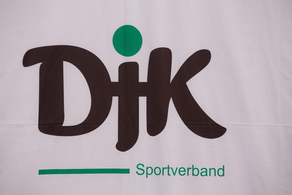 Logo des DJK Sportverbands mit stilisierten Buchstaben in Schwarz und einem gr&uuml;nen Punkt dar&uuml;ber.