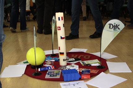 Anordnung von Werbematerialien, einer gelben Kugel und einem aufrechten Kerzenst&auml;nder auf einem roten Teppich.